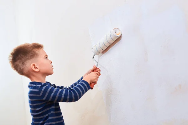 小男孩在家居装修过程中用油漆辊粉刷墙的侧视图 — 图库照片