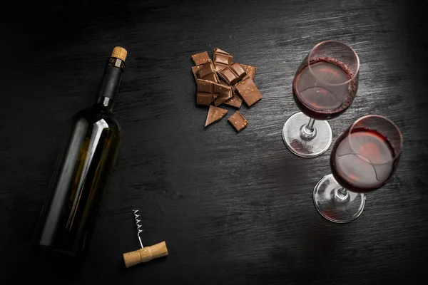 Kırmızı şarap ile bir tirbuşon bir şişe. Siyah bir ahşap arka plan üzerinde.