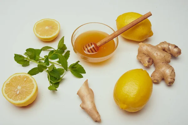 close up of honey at bowl, ginger, lemon and mint on white table