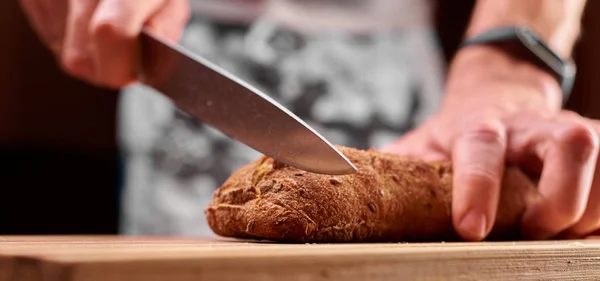 Whole grain bread put on kitchen wood plate with a chef holding gold knife for cut. Fresh bread on table close-up. Fresh bread on the kitchen table The healthy eating and traditional bakery concept