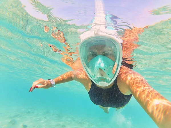 woman in diving mask taking selfie while swimming under water