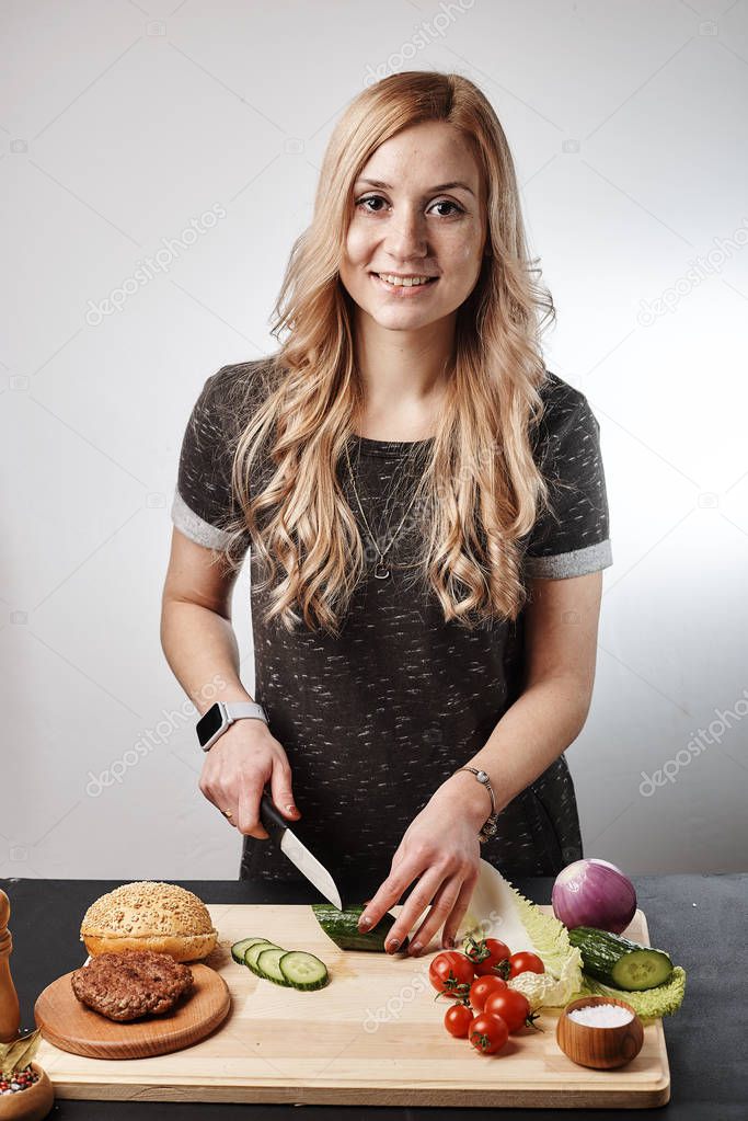 Blond smiling woman making burger at table