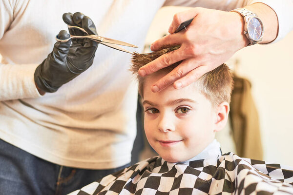Partial view of barber making haircut of little boy at salon
