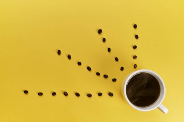 Fincan ve sarı arka plan üzerinde kavrulmuş aromatik kahve çekirdekleri