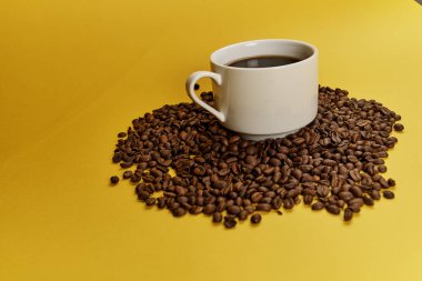 Fincan ve sarı arka plan üzerinde kavrulmuş aromatik kahve çekirdekleri