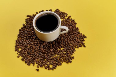 Fincan ve sarı arka plan üzerinde kavrulmuş aromatik kahve çekirdekleri