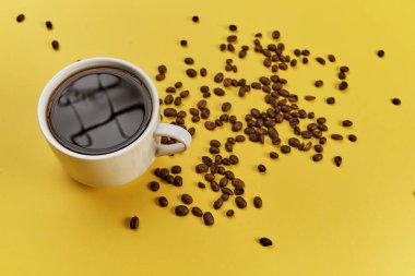 Fincan ve sarı arka plan üzerinde kavrulmuş aromatik kahve çekirdekleri