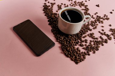 Akıllı telefon, fincan ve pembe arka plan üzerinde kavrulmuş aromatik kahve çekirdekleri
