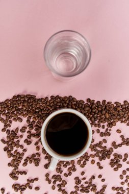 Pembe arka planda bir fincan su, kahve fincanı ve kavrulmuş aromatik kahve çekirdekleri