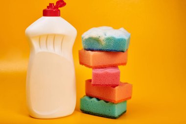 Sarı arka planda temizleyici şişe ve köpüklü yıkama süngerleri