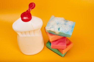 Sarı arka planda temizleyici şişe ve köpüklü yıkama süngerleri