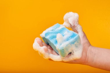 Sarı arka planda köpüklü yıkama süngeri tutan adamın kısmi görünümü