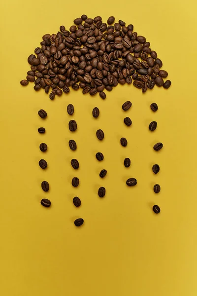 Cloud with rain made of roasted coffee beans on yellow background