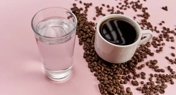 Pembe arka planda bir fincan su, kahve fincanı ve kavrulmuş aromatik kahve çekirdekleri