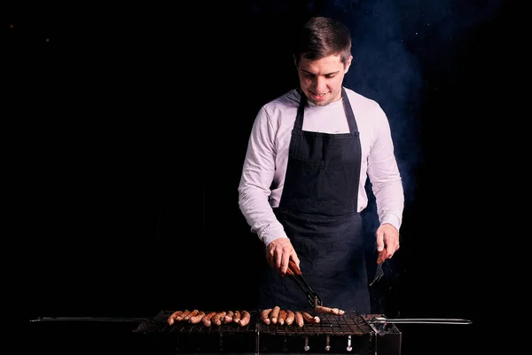 Young man grilling sausages outdoors