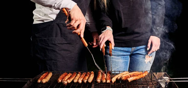 Partial shot of couple grilling sausages outdoors