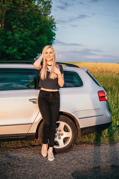 自然の上に車の近くに立っている美しい若い女性の肖像画 — ストック写真