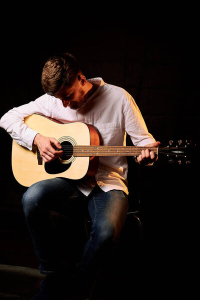 portrait of handsome man with acoustic guitar on black