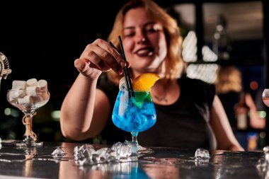 Barda mavi kokteyl yapan genç sarışın barmen kadın.