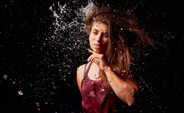 Splashes of water on the young woman on dark background