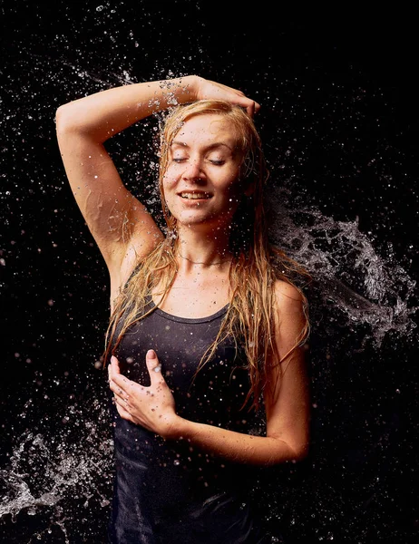 Splashes of water on the young woman on dark background