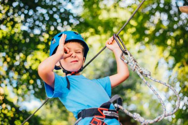 Küçük sevimli çocuk bir yaz güneşli bir günde bir tırmanma macera parkı aktivite zevk. Kask ve sigorta ile ekstrem spor tırmanma