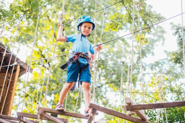 Küçük sevimli çocuk bir yaz güneşli bir günde bir tırmanma macera parkı aktivite zevk. Kask ve sigorta ile ekstrem spor tırmanma