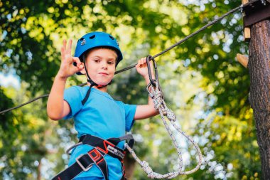 Küçük sevimli çocuk bir yaz güneşli bir günde bir tırmanma macera parkı aktivite zevk. Kask ve sigorta ile ekstrem spor tırmanma