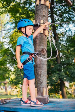 Küçük sevimli çocuk bir yaz güneşli bir günde bir tırmanma macera parkı aktivite zevk. Kask ve sigorta ile ekstrem spor tırmanma