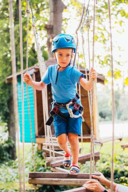 Küçük sevimli çocuk bir yaz güneşli bir günde bir tırmanma macera parkı aktivite zevk. Kask ve sigorta ile ekstrem spor tırmanma