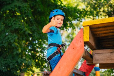 Küçük sevimli çocuk bir yaz güneşli bir günde bir tırmanma macera parkı aktivite zevk. Kask ve sigorta ile ekstrem spor tırmanma