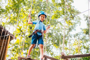 Küçük sevimli çocuk bir yaz güneşli bir günde bir tırmanma macera parkı aktivite zevk. Kask ve sigorta ile ekstrem spor tırmanma