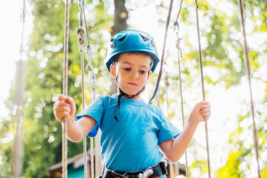 Küçük sevimli çocuk bir yaz güneşli bir günde bir tırmanma macera parkı aktivite zevk. Kask ve sigorta ile ekstrem spor tırmanma