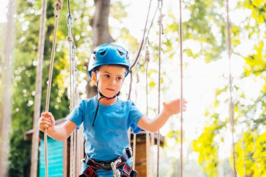 Küçük sevimli çocuk bir yaz güneşli bir günde bir tırmanma macera parkı aktivite zevk. Kask ve sigorta ile ekstrem spor tırmanma