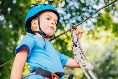Küçük sevimli çocuk bir yaz güneşli bir günde bir tırmanma macera parkı aktivite zevk. Kask ve sigorta ile ekstrem spor tırmanma