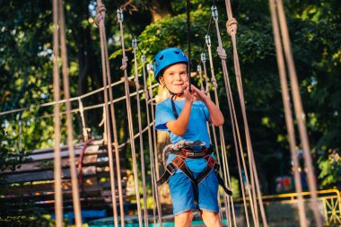 Küçük sevimli çocuk bir yaz güneşli bir günde bir tırmanma macera parkı aktivite zevk. Kask ve sigorta ile ekstrem spor tırmanma