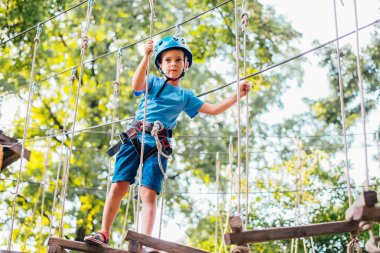 Küçük sevimli çocuk bir yaz güneşli bir günde bir tırmanma macera parkı aktivite zevk. Kask ve sigorta ile ekstrem spor tırmanma