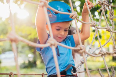 Küçük sevimli çocuk bir yaz güneşli bir günde bir tırmanma macera parkı aktivite zevk. Kask ve sigorta ile ekstrem spor tırmanma