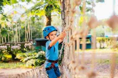 Küçük sevimli çocuk bir yaz güneşli bir günde bir tırmanma macera parkı aktivite zevk. Kask ve sigorta ile ekstrem spor tırmanma