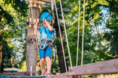 Küçük sevimli çocuk bir yaz güneşli bir günde bir tırmanma macera parkı aktivite zevk. Kask ve sigorta ile ekstrem spor tırmanma