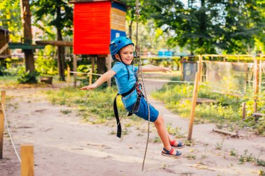 Küçük sevimli çocuk bir yaz güneşli bir günde bir tırmanma macera parkı aktivite zevk. Kask ve sigorta ile ekstrem spor tırmanma
