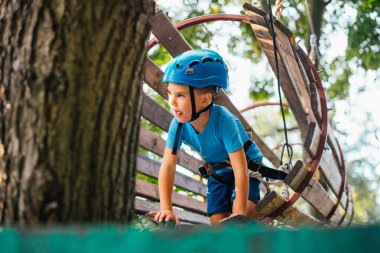 Küçük sevimli çocuk bir yaz güneşli bir günde bir tırmanma macera parkı aktivite zevk. Kask ve sigorta ile ekstrem spor tırmanma