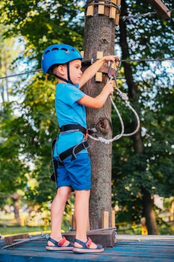 Küçük sevimli çocuk bir yaz güneşli bir günde bir tırmanma macera parkı aktivite zevk. Kask ve sigorta ile ekstrem spor tırmanma