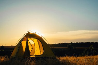 Gün doğumunda dağlarda çayır arasında kampta turist çadırı