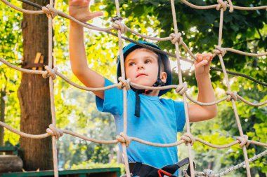 Küçük sevimli çocuk bir yaz güneşli bir günde bir tırmanma macera parkı aktivite zevk. Kask ve sigorta ile ekstrem spor tırmanma