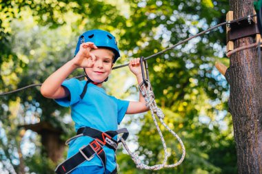 Küçük sevimli çocuk bir yaz güneşli bir günde bir tırmanma macera parkı aktivite zevk. Kask ve sigorta ile ekstrem spor tırmanma