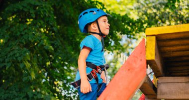 Küçük sevimli çocuk bir yaz güneşli bir günde bir tırmanma macera parkı aktivite zevk. Kask ve sigorta ile ekstrem spor tırmanma
