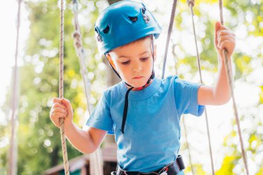 Küçük sevimli çocuk bir yaz güneşli bir günde bir tırmanma macera parkı aktivite zevk. Kask ve sigorta ile ekstrem spor tırmanma