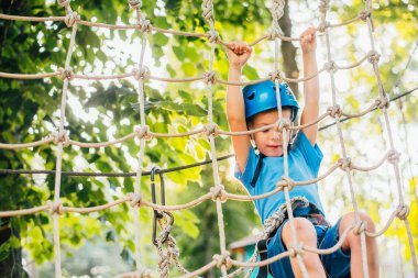 Küçük sevimli çocuk bir yaz güneşli bir günde bir tırmanma macera parkı aktivite zevk. Kask ve sigorta ile ekstrem spor tırmanma