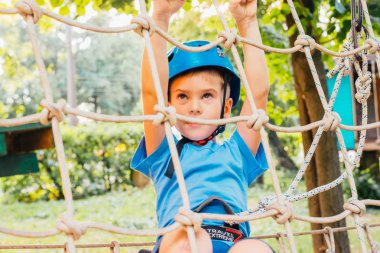 Küçük sevimli çocuk bir yaz güneşli bir günde bir tırmanma macera parkı aktivite zevk. Kask ve sigorta ile ekstrem spor tırmanma